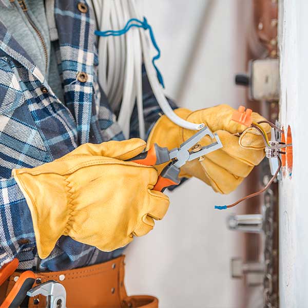 Electricista con guantes amarillos usando una herramienta para cortar cables dentro de una caja de conexiones en la pared.